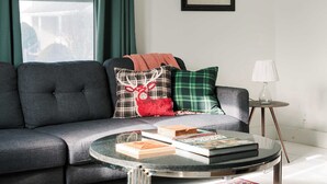 Ett modernt vardagsrum med en grå soffa, ett runt soffbord i glas och en mönstrad matta.
