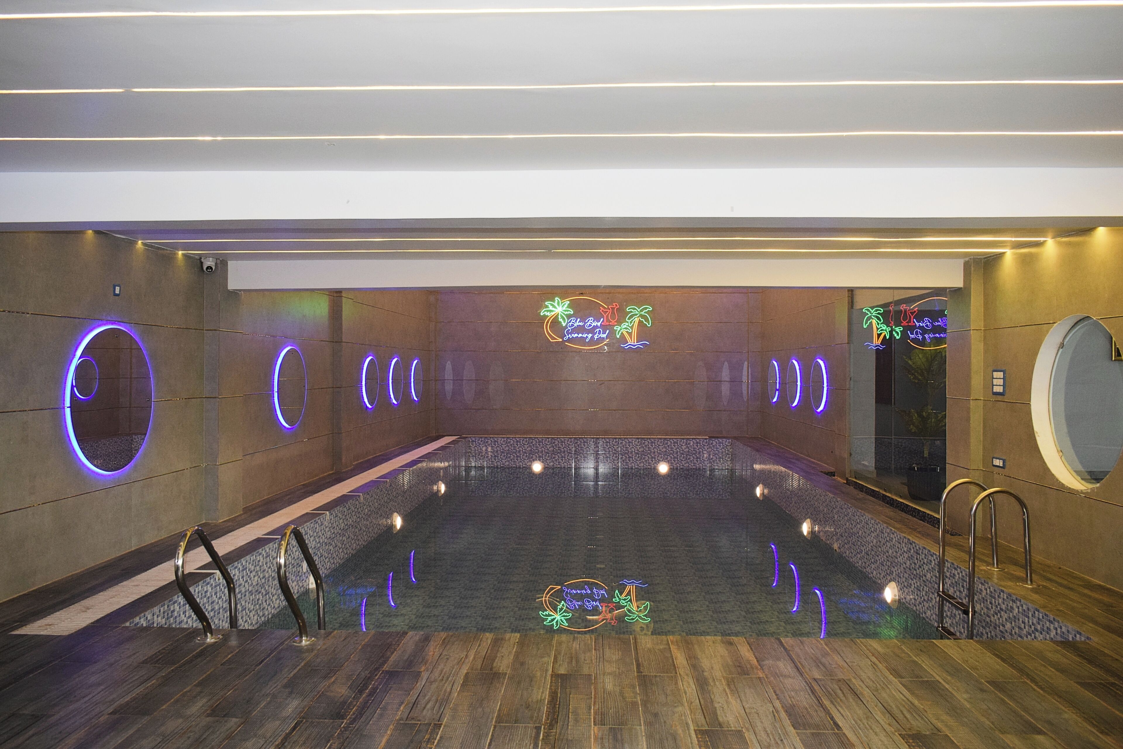 A modern indoor swimming pool with neon signs, wooden flooring, and a central island.