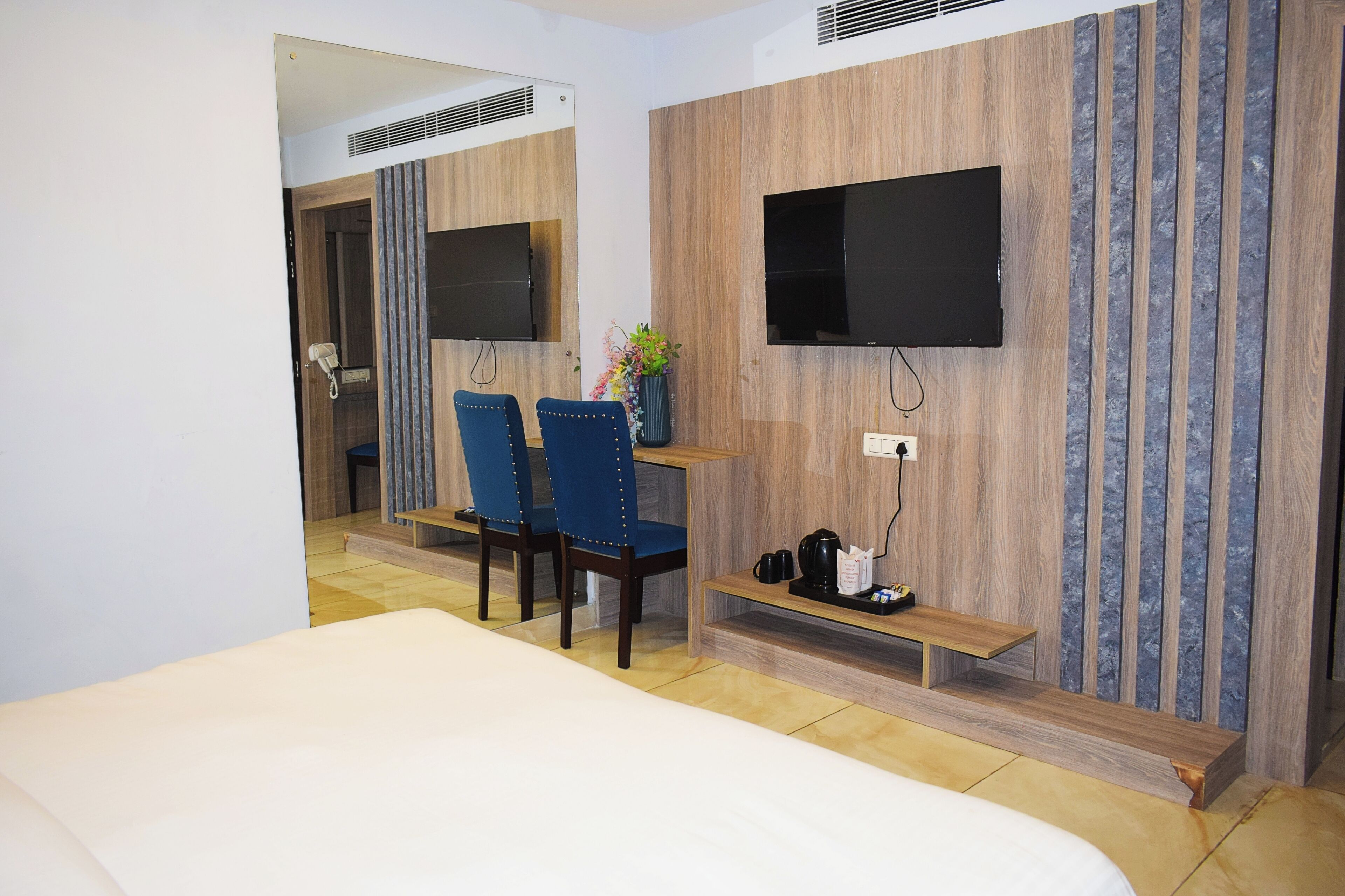 Une chambre d’hôtel comprenant un lit, un bureau avec deux chaises, un téléviseur fixé au mur et une petite étagère avec une machine à café.
