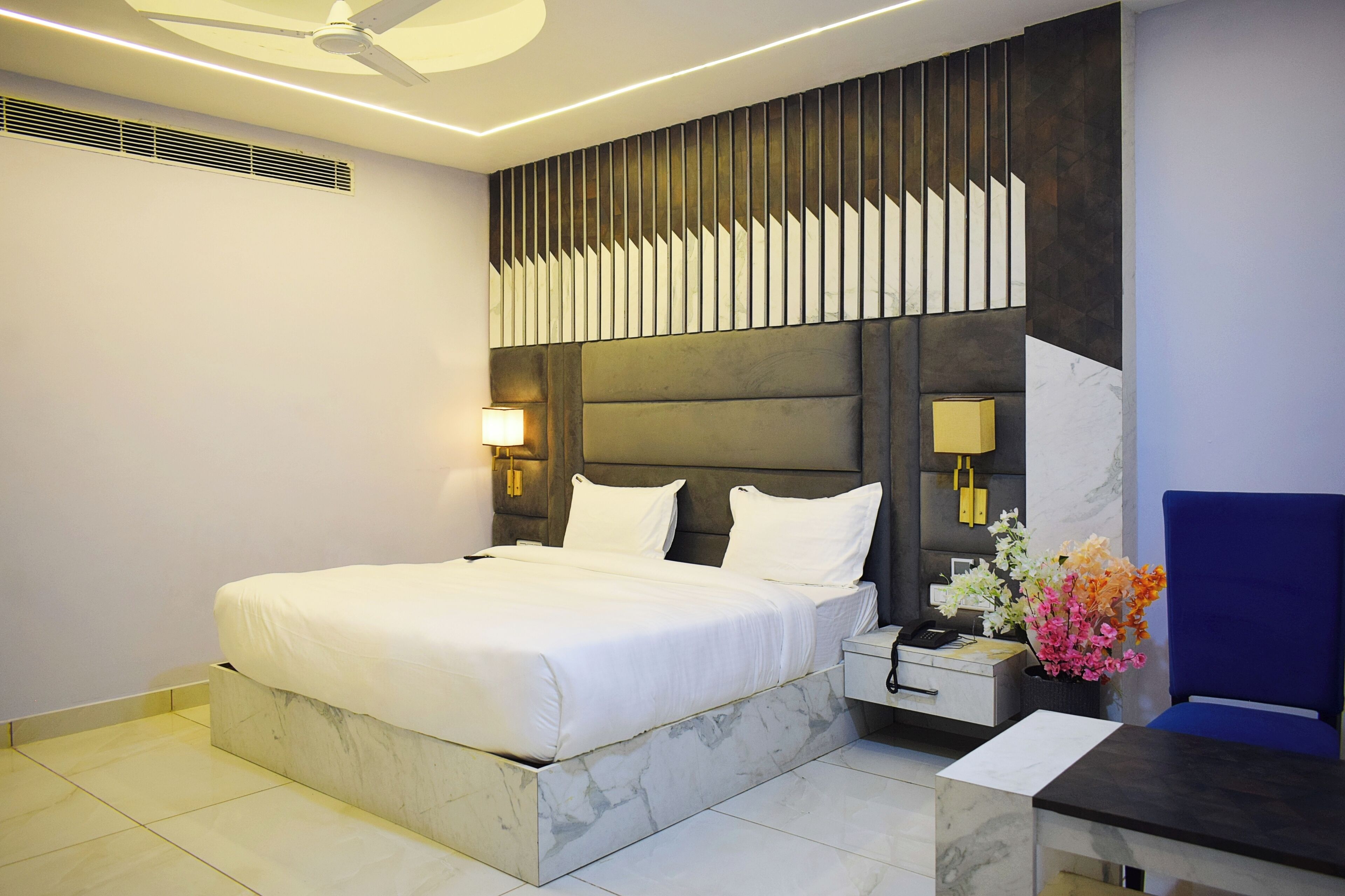 A modern hotel room with a large bed, a desk with a chair, and a decorative wall panel.