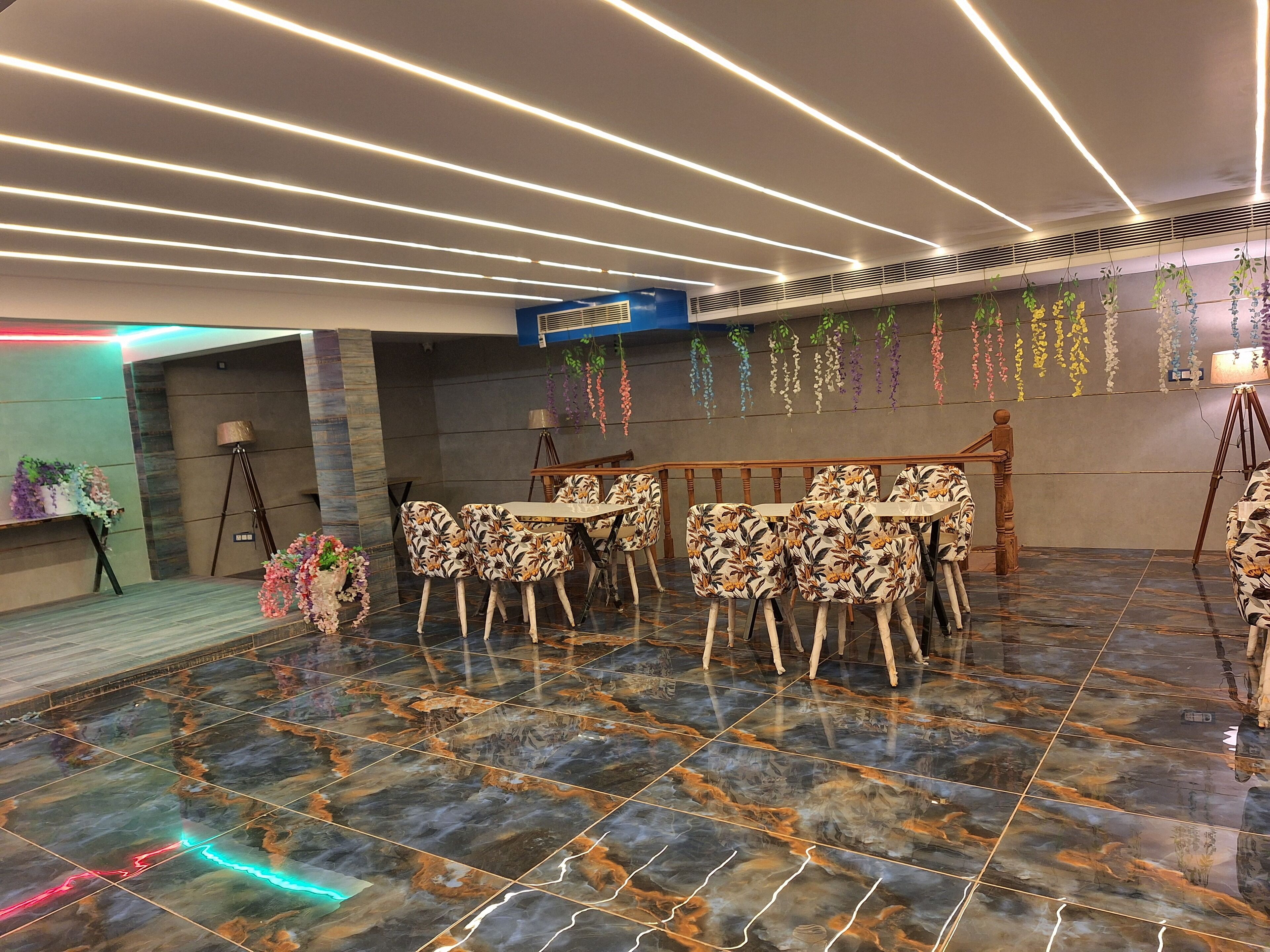 A dining area with a marble floor, a table with floral chairs, and decorative hanging plants.