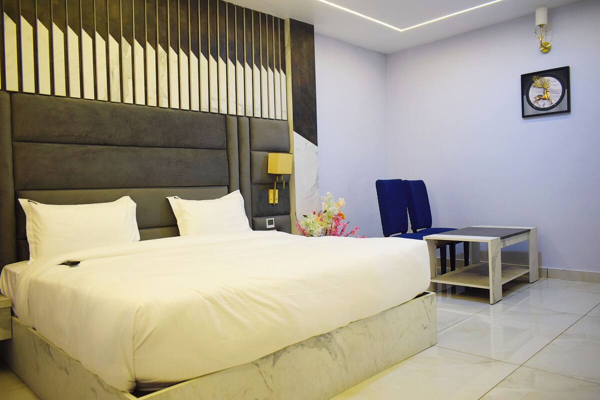A modern hotel room with a large bed, a small table, a chair, and a decorative wall piece.