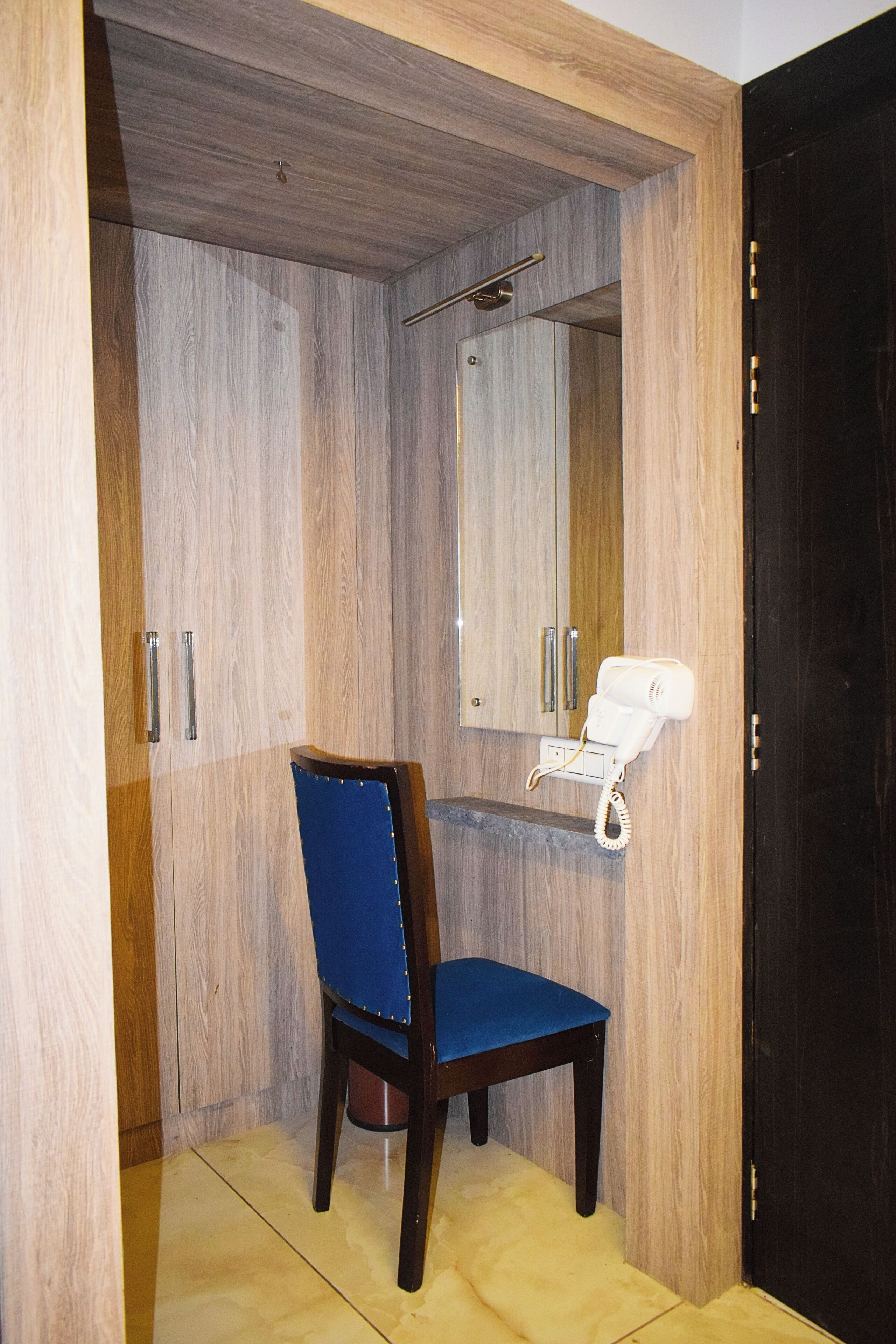 Un baño con tocador de madera, una silla azul y un secador de pelo blanco sobre una estantería.