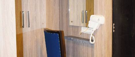 Un baño con tocador de madera, una silla azul y un secador de pelo blanco sobre una estantería.
