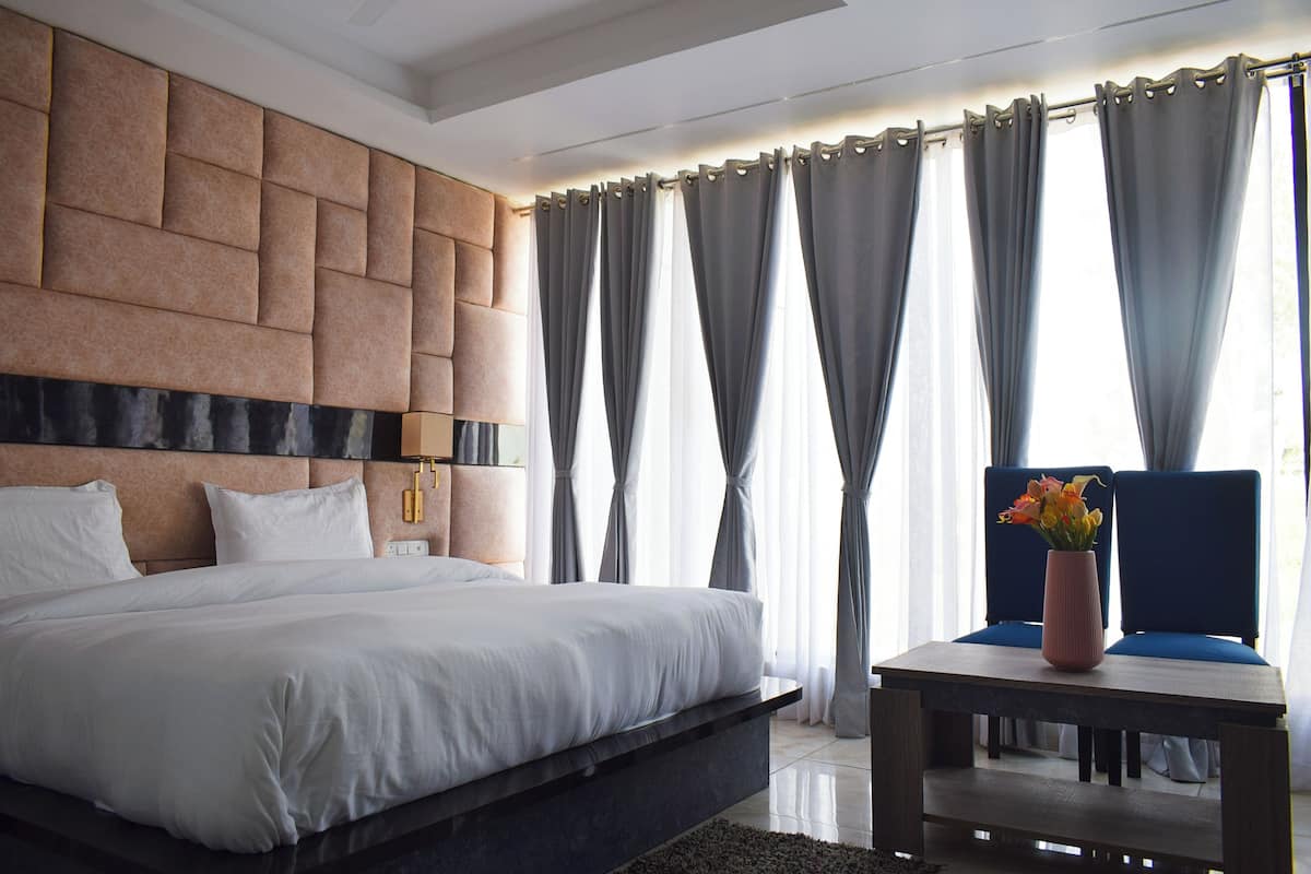 A modern hotel room with a large bed, a wooden nightstand, and a vase of flowers.