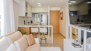 Un salon moderne avec un canapé, une table basse et un coin repas, la cuisine étant visible au fond.