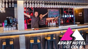 A bar area with a coffee machine, wine glasses, and bottles. There are bar stools and a chalkboard menu. - Apart Hotel des Cols  (Borderes-Louron)