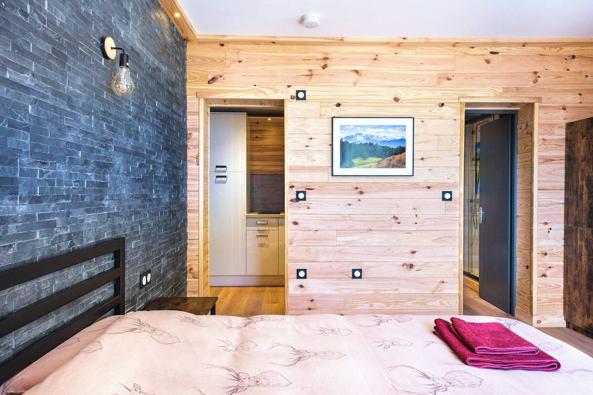 A bedroom with a bed, a wooden wall, a picture, and a bathroom door.