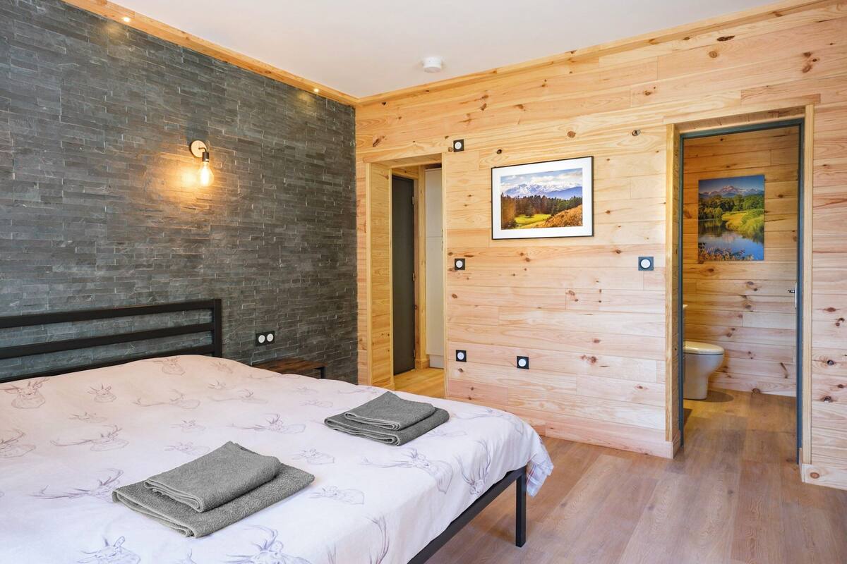 A modern bedroom with a bed, a wooden wall, a picture, and a door leading to a bathroom.