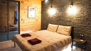 A bedroom with a bed, wooden walls, a stone accent wall, and a small bedside table. - Apart Hotel des Cols  (Borderes-Louron)
