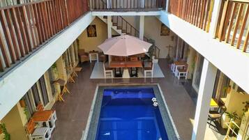 A multi-level indoor swimming pool area with a central pool, seating around the pool, and a staircase leading to an upper level.
