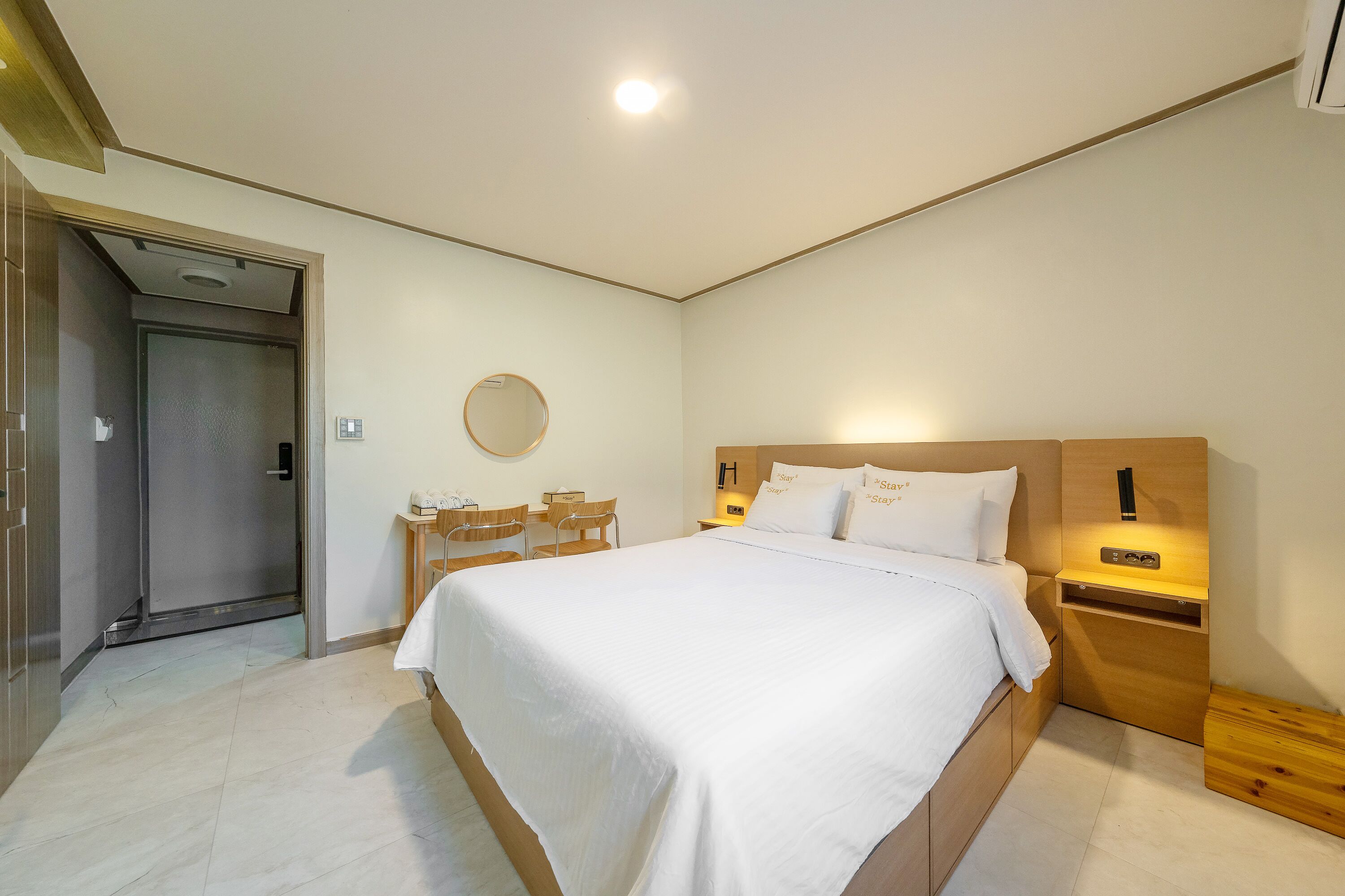 Un dormitorio moderno con una cama grande, mesitas de noche, un espejo redondo y un cabecero de madera.