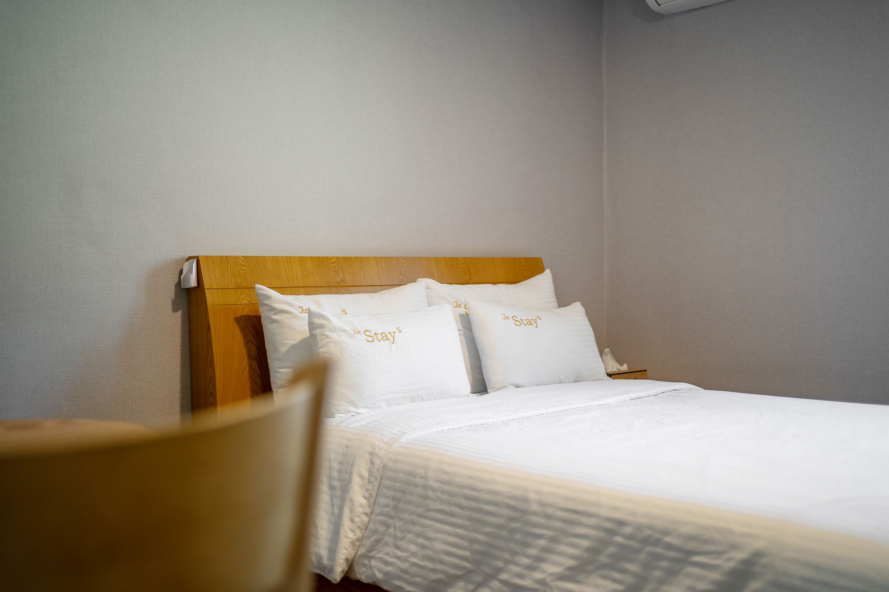 A neatly made bed with white bedding and pillows, a wooden headboard, and a small bedside table with a tissue box.
