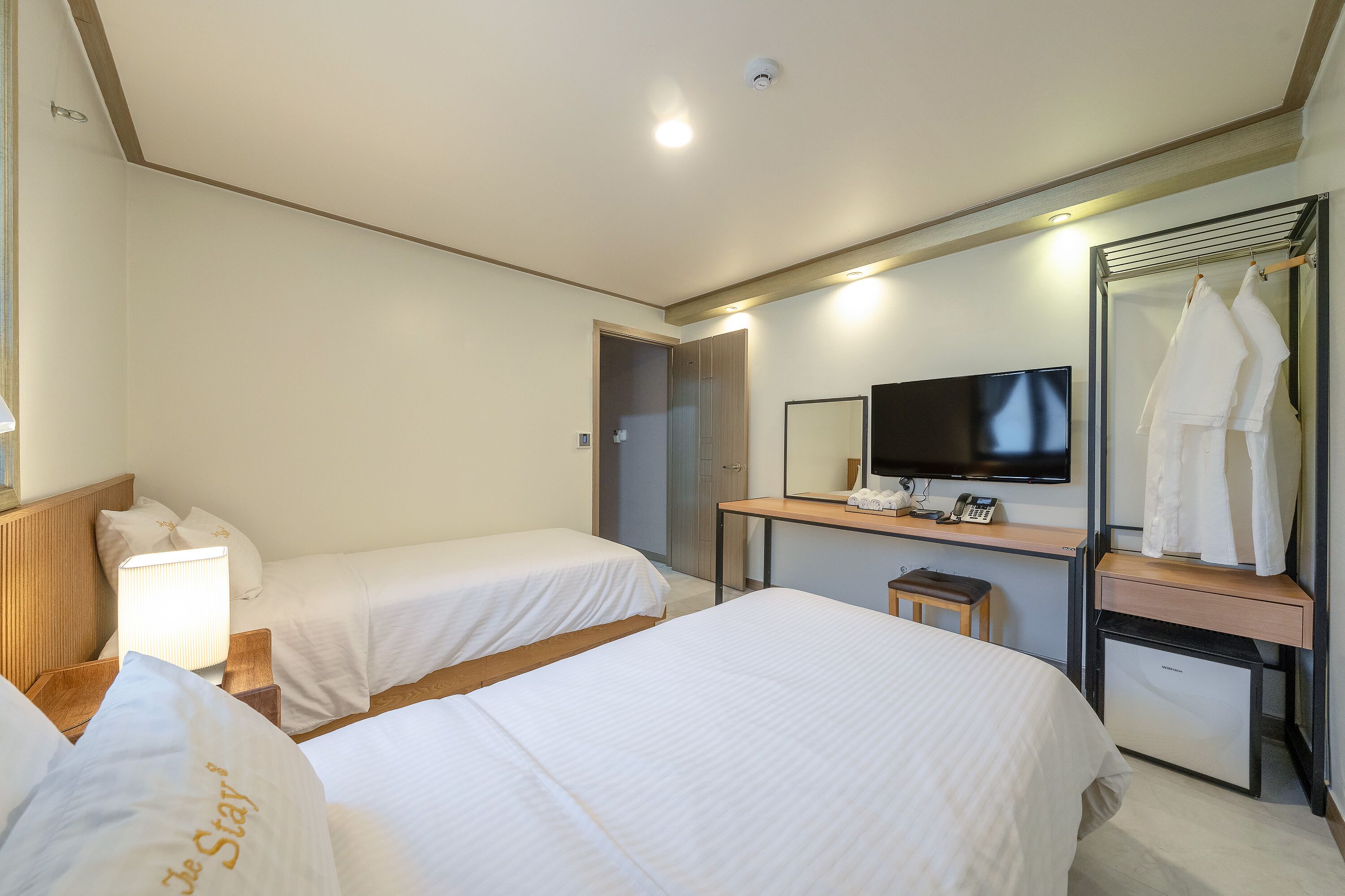 Habitación de hotel con dos camas, un escritorio con televisor y un espejo.