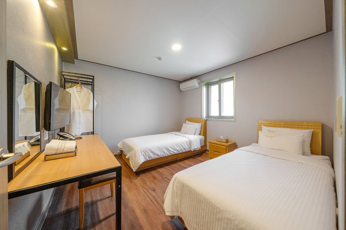 A hotel room with two single beds, a wooden desk, a mirror, and a window.