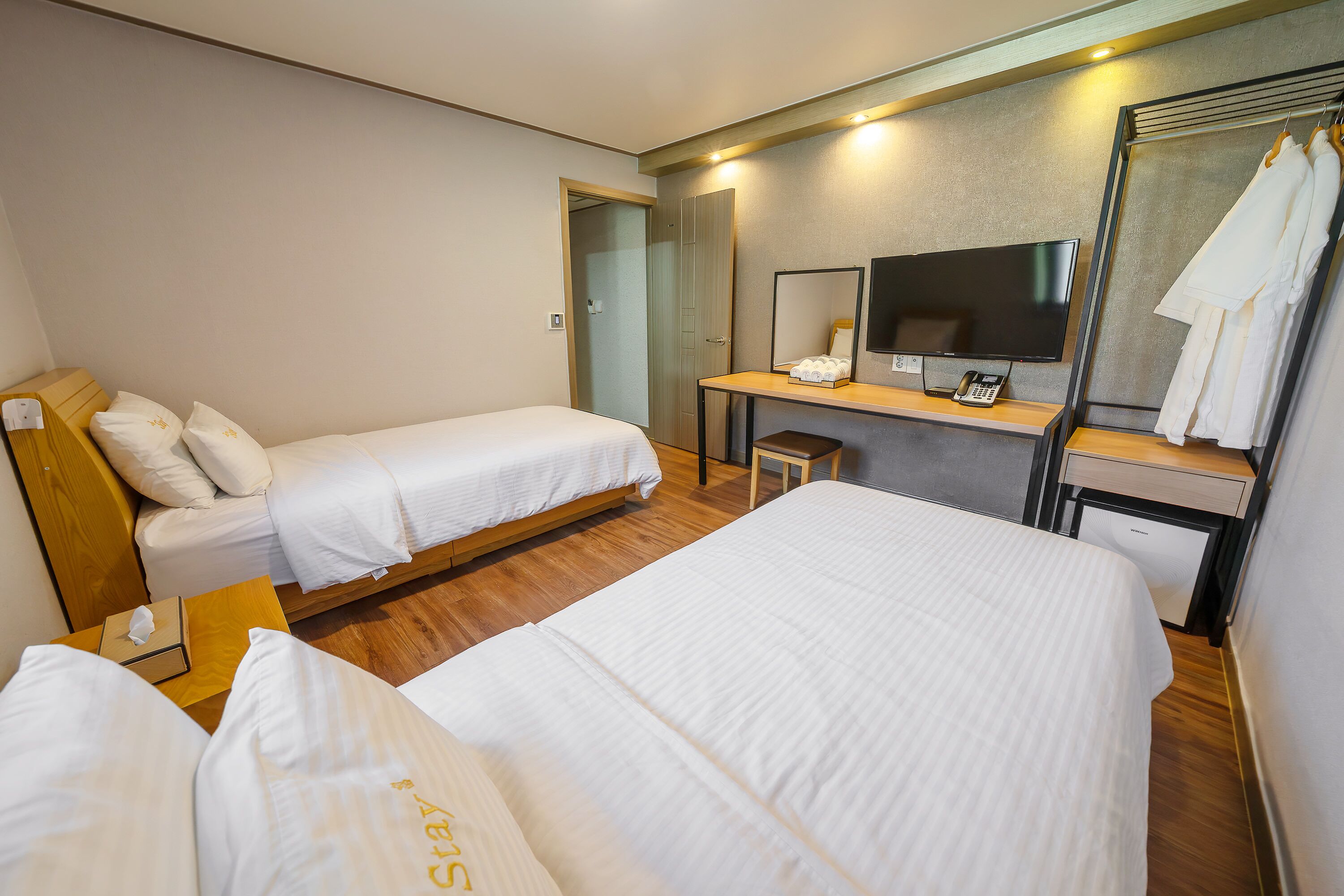 A hotel room with two single beds, a desk with a TV, a mirror, and a wardrobe.