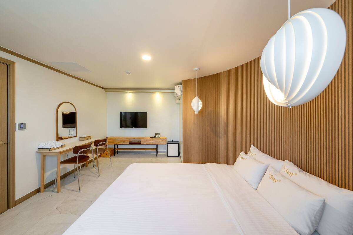 A hotel room with a large bed, a desk with chairs, a television, and a unique wall-mounted light fixture.