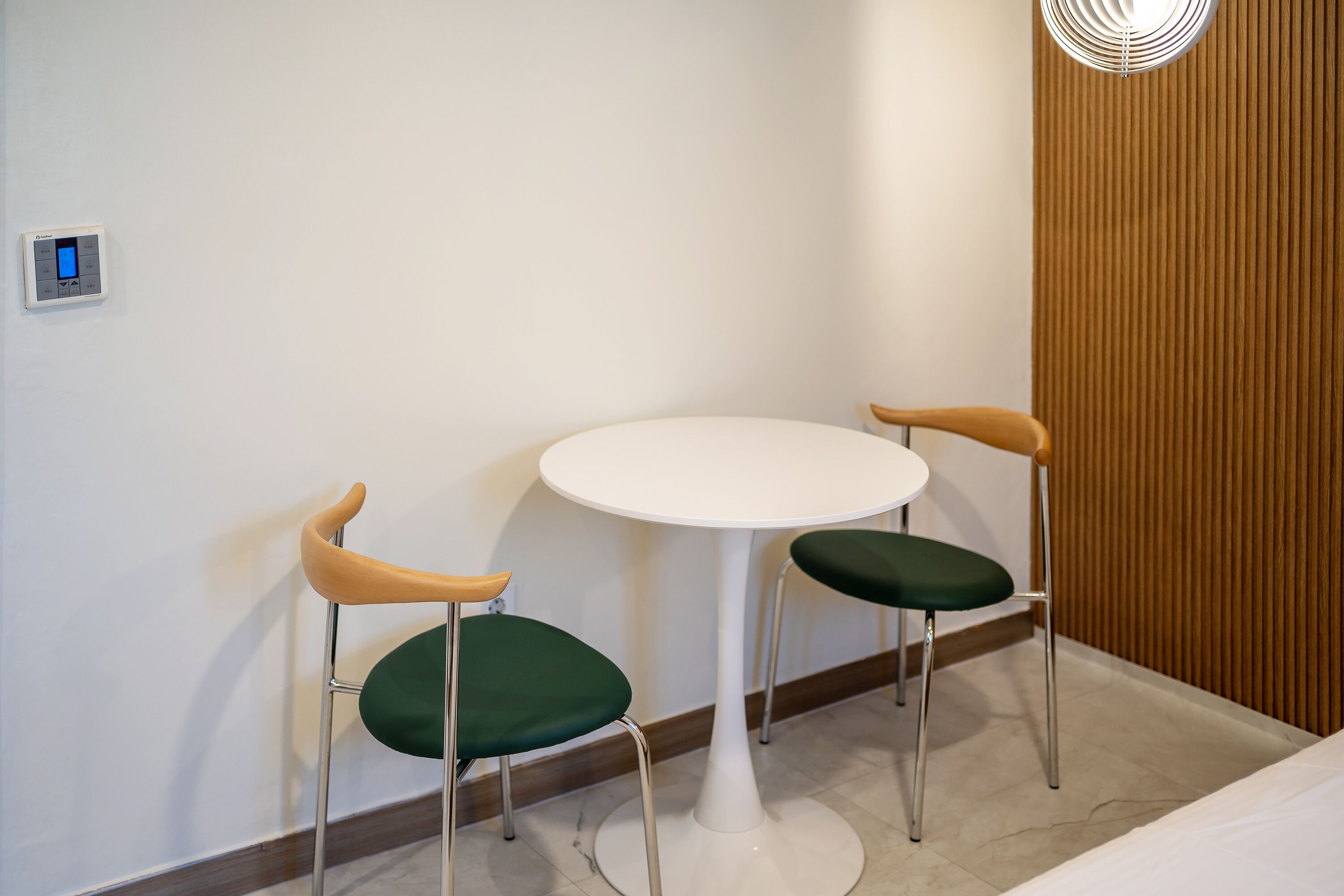 A small, modern room with a white round table and two chairs with green cushions.