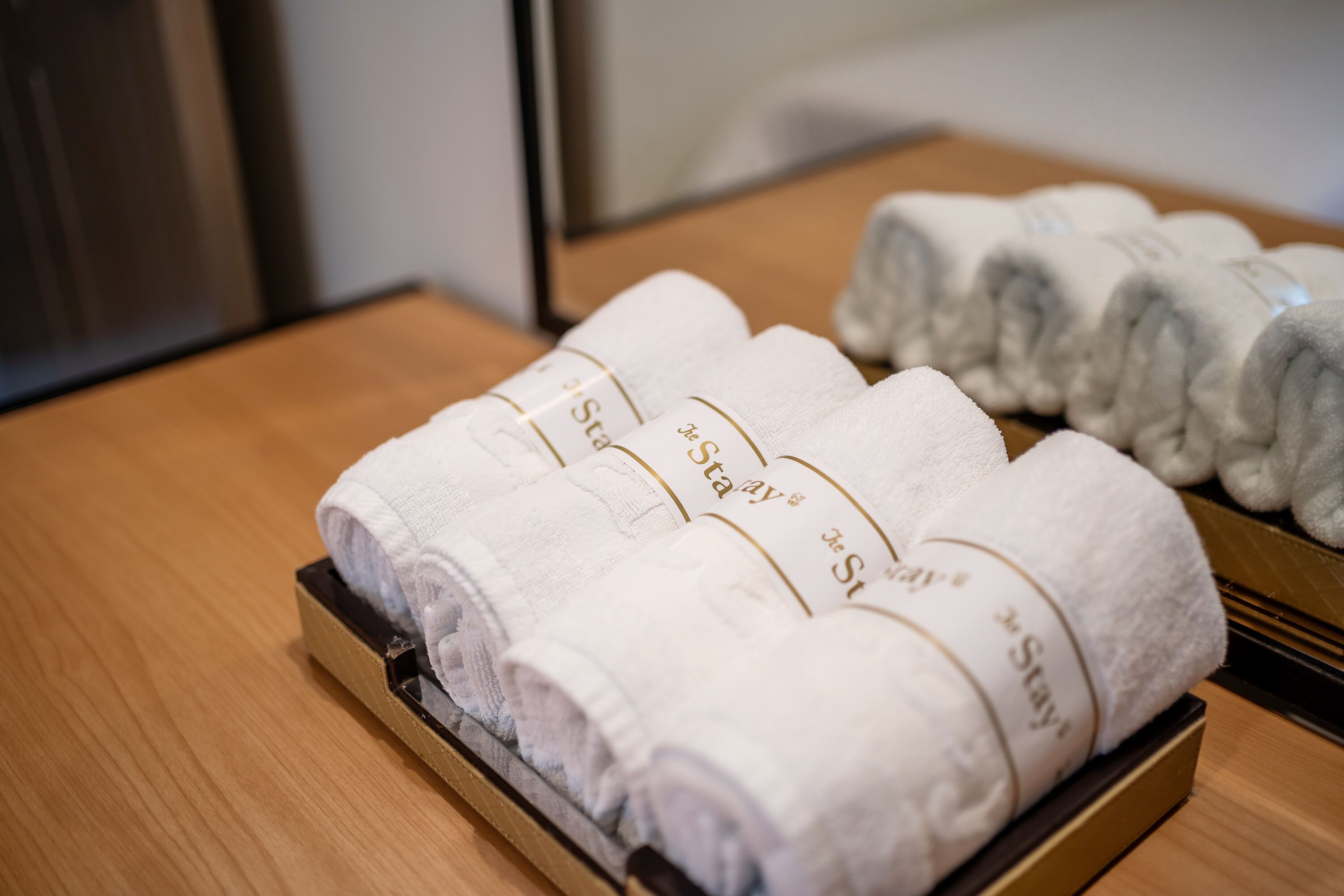 Neatly folded white towels with "Stay" printed on them, placed on a wooden tray.