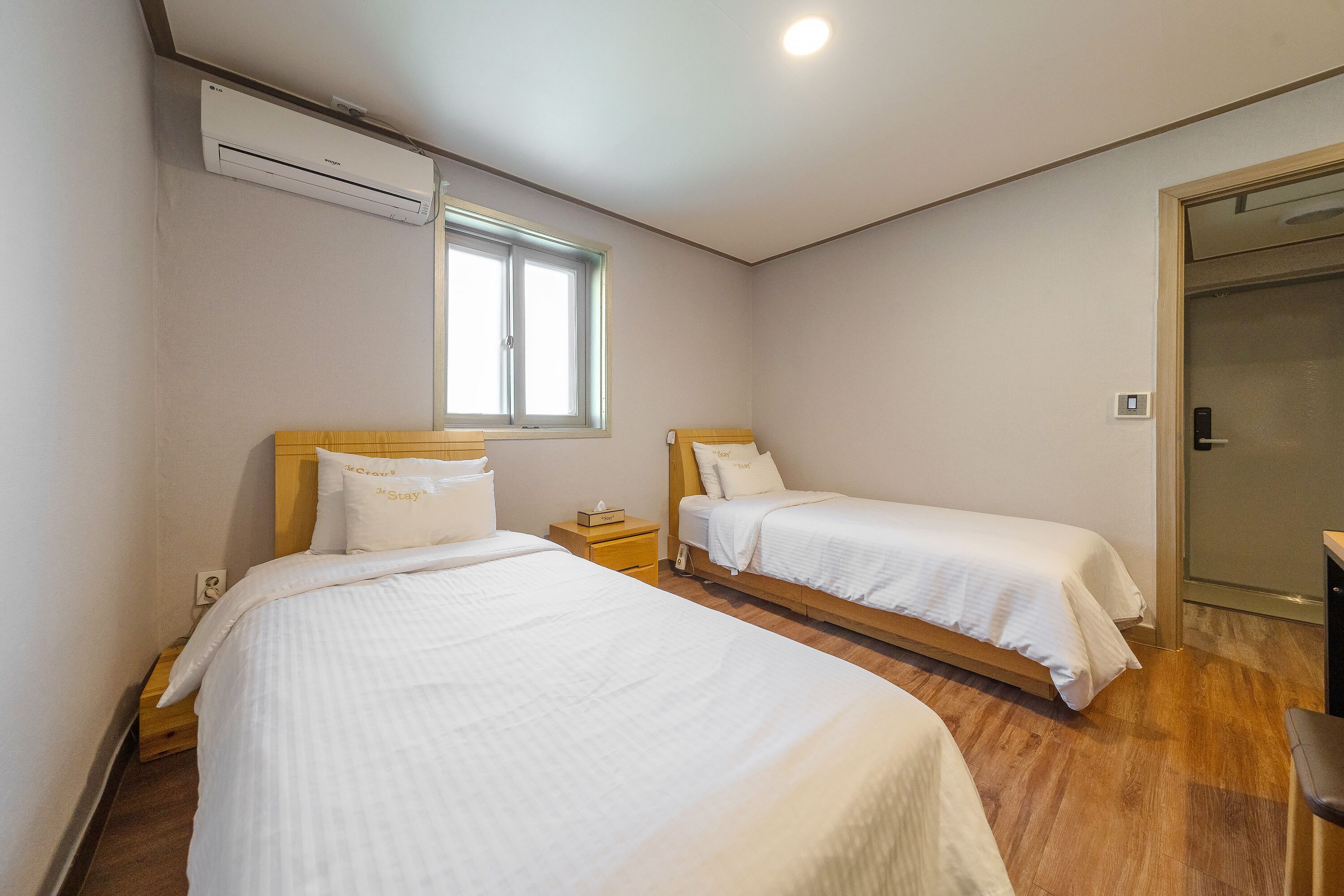 Une chambre d’hôtel avec deux lits, une fenêtre, un appareil de climatisation et une porte.