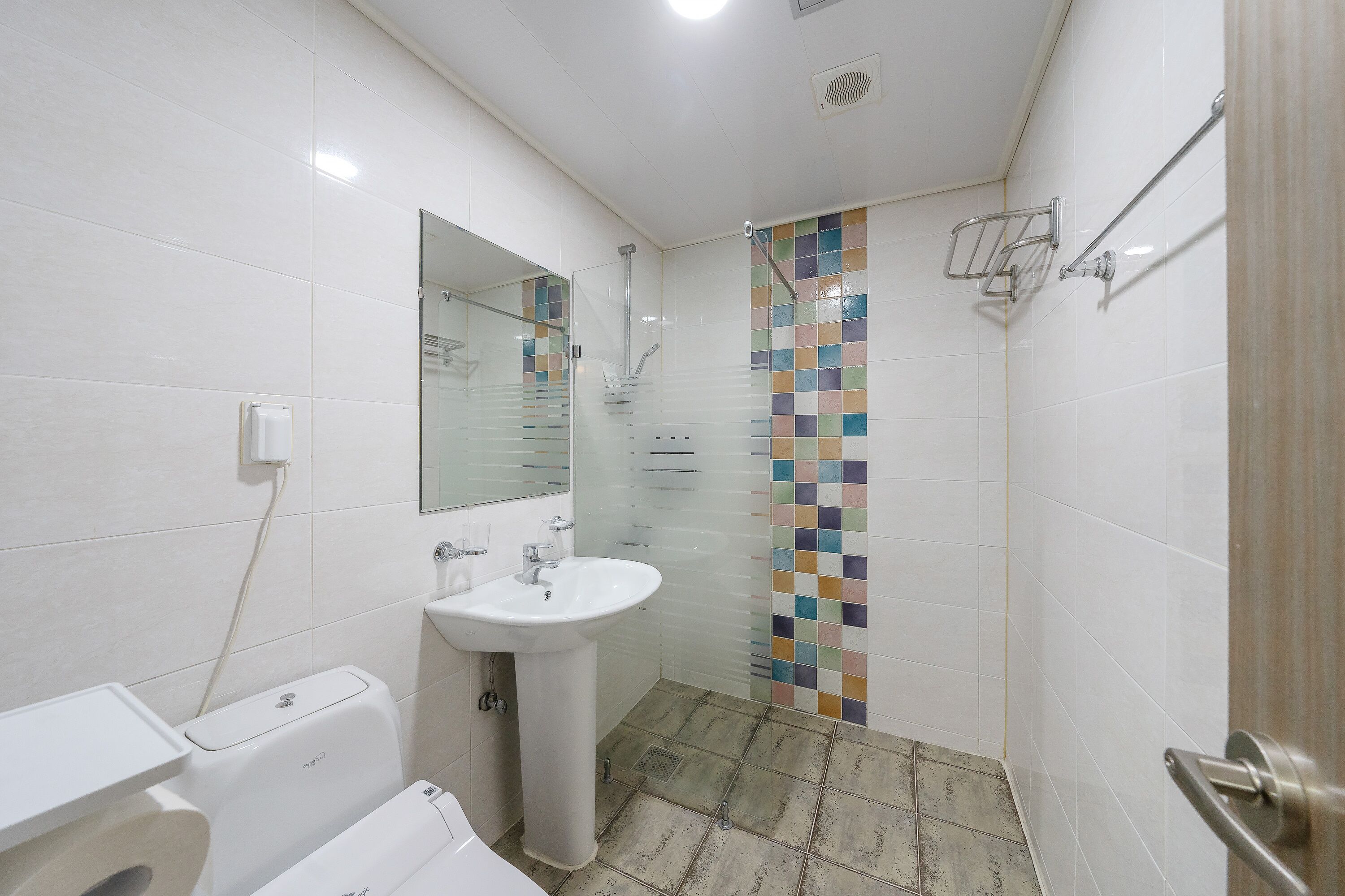 Un baño con un lavabo blanco, inodoro, ducha con pared de azulejos y espejo.