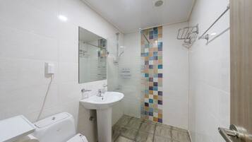 Un baño con un lavabo blanco, inodoro, ducha con pared de azulejos y espejo.