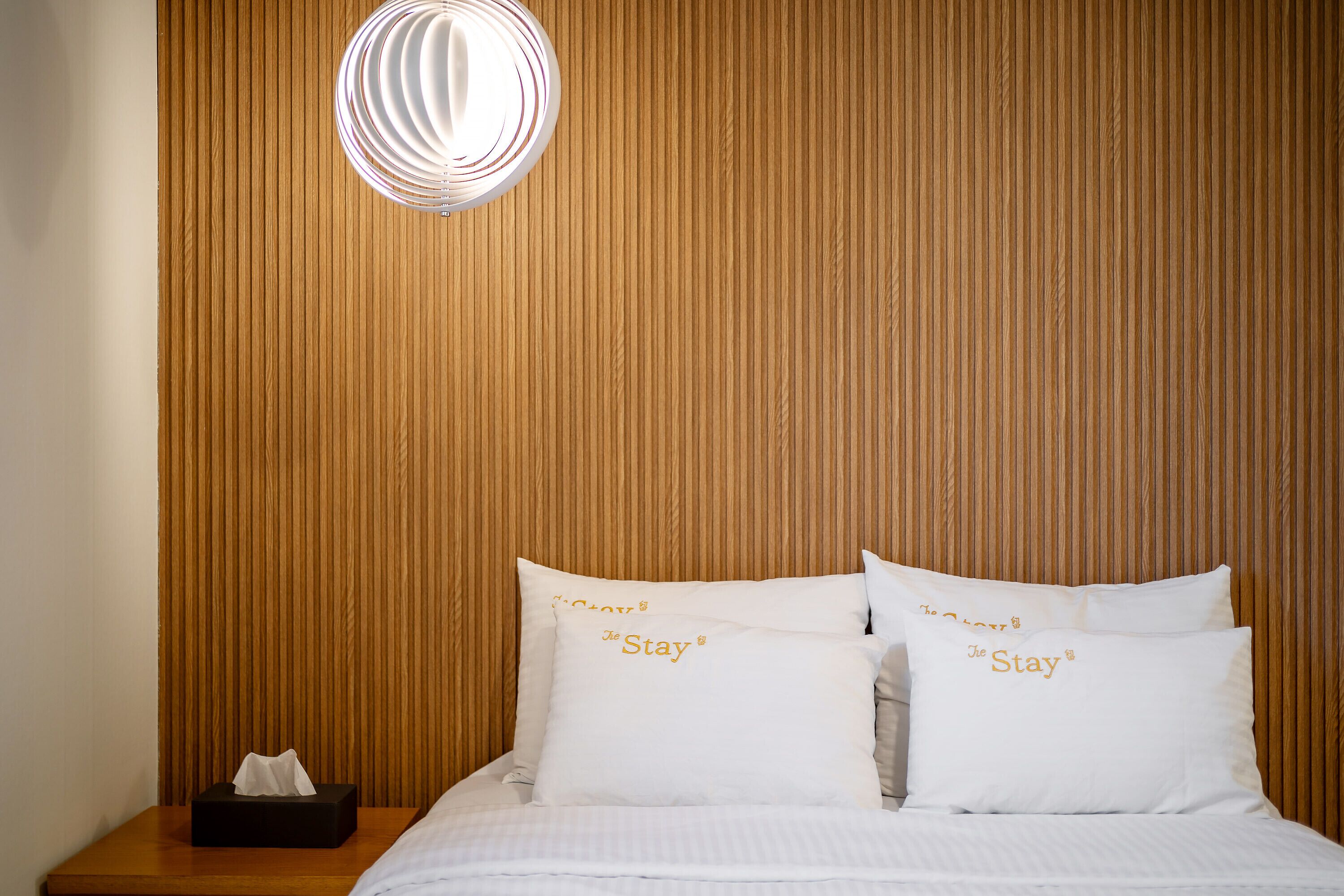 A neatly made bed with two pillows, a bedside table with a tissue box, and a wall-mounted light fixture.