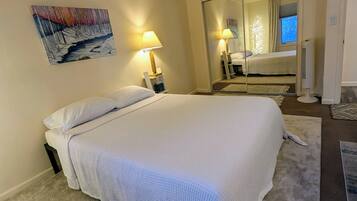 A neatly made bed with white linens, a bedside lamp, and a painting on the wall.