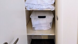Un armario con repisas que contiene cajas de almacenamiento de plástico y ropa blanca doblada.