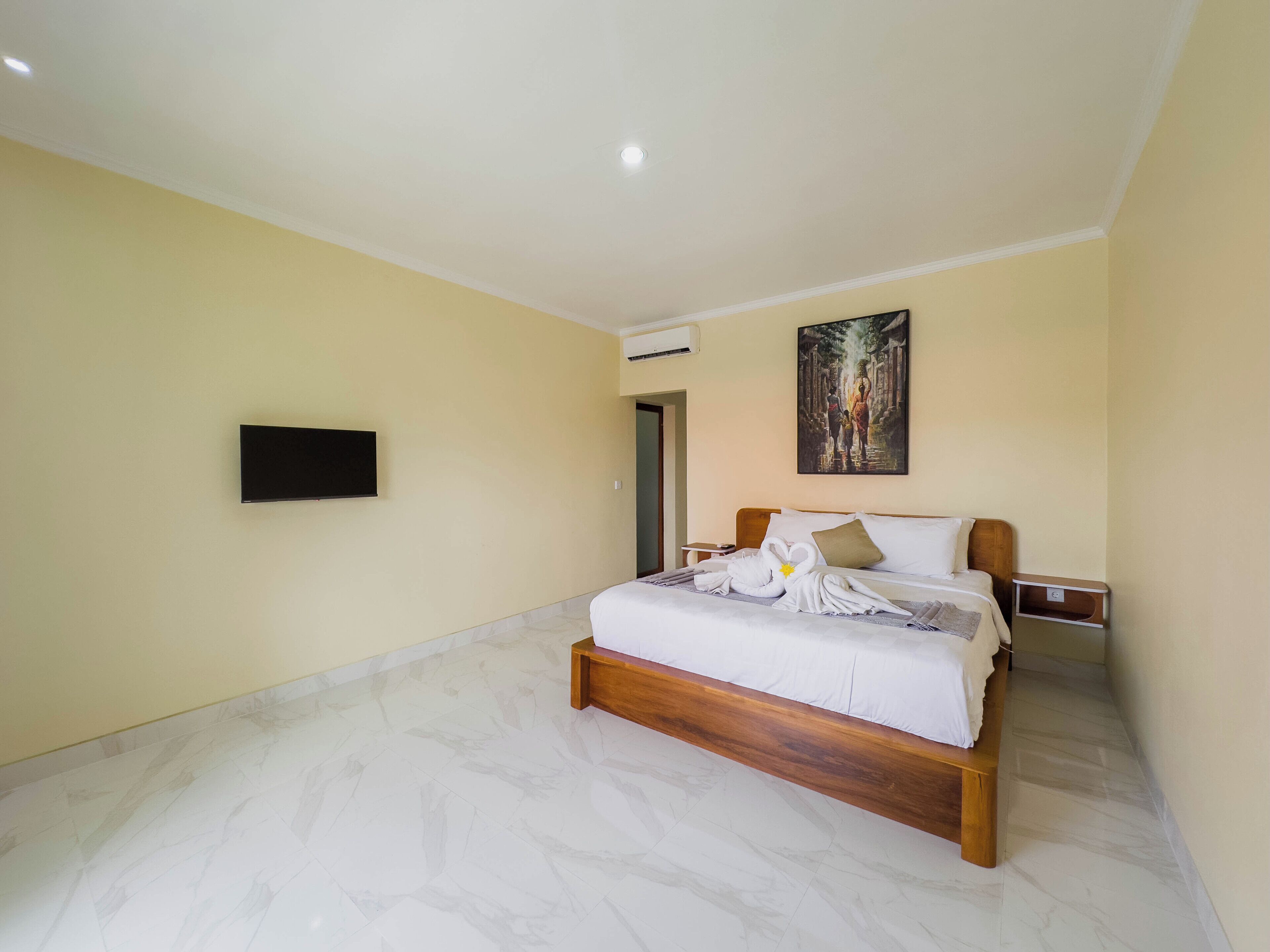 A hotel room with a bed, a flat-screen TV, and a painting on the wall.