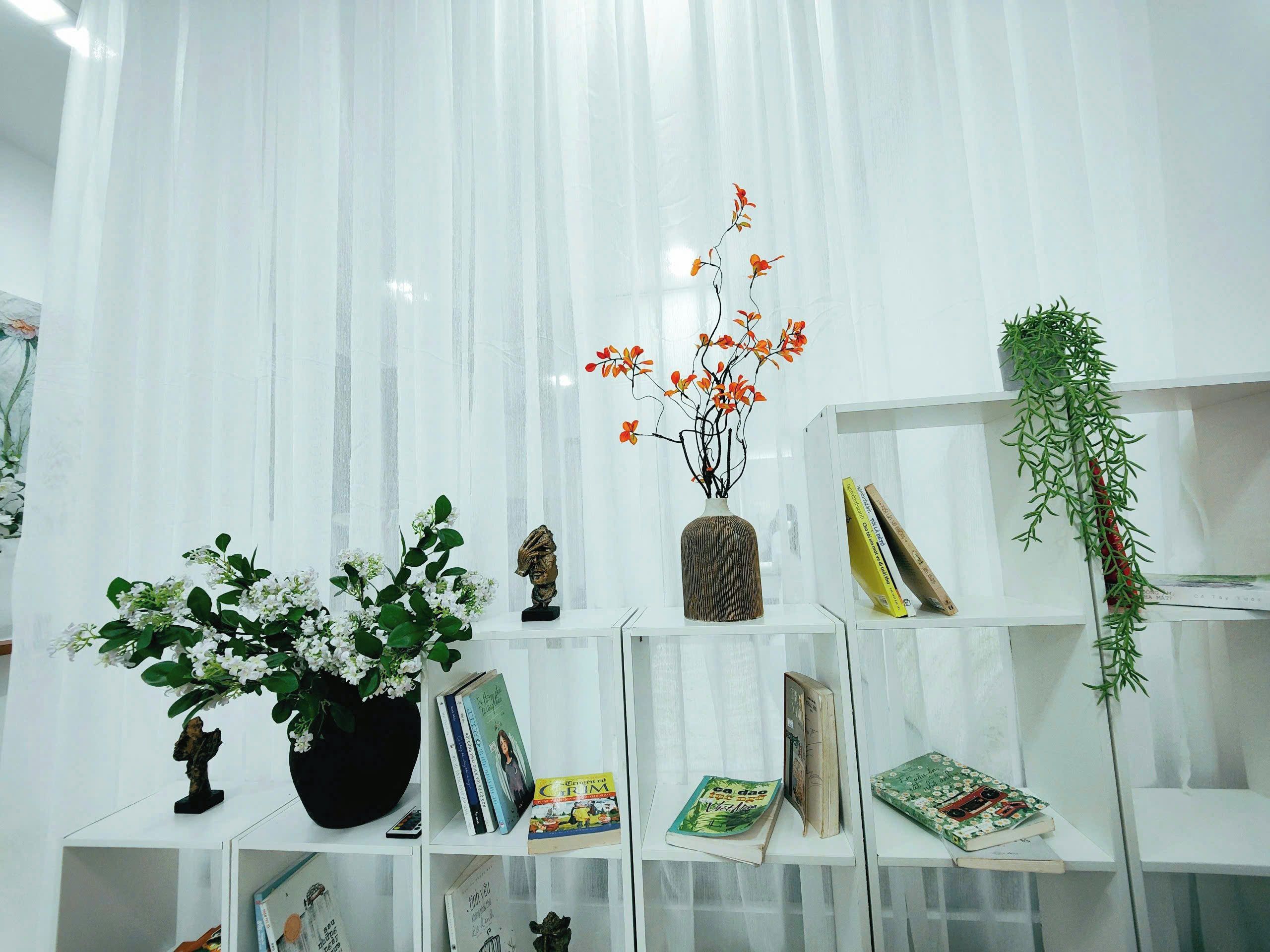 Une pièce avec des rideaux blancs, une plante en pot, une sculpture et des livres sur des étagères.