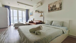 Habitación de hotel con una cama grande, un sofá, un escritorio y vistas a la ciudad a través de amplios ventanales.