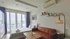 Una habitación de hotel moderna con cama, sofá, una pequeña mesa, escritorio, lámpara y vistas a la ciudad.