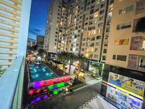 A high-rise building with multiple balconies, a swimming pool with colorful lighting, and a view of the surrounding urban area. - Studio 2-beds Apartment (Ho Chi Minh City)