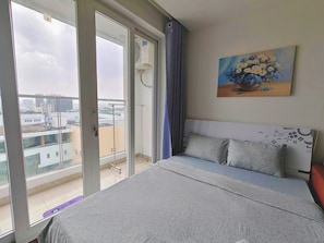 Une chambre à coucher avec un lit, un tableau, une fenêtre et une vue sur des immeubles.