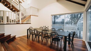 A dining area with a wooden table and chairs, a staircase with white railings, and a large window with a view of trees and a white fence. - The Vintners: Where luxury meets nature, five master suites & spacious living (Peerabeelup)