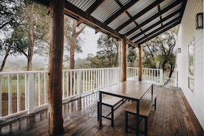 Un espace extérieur abrité, doté d’une table et de bancs en bois, entouré de rampes blanches et d’arbres.