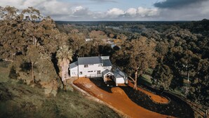 A large white house with a driveway and a small structure, surrounded by dense forest and hills. - The Vintners: Where luxury meets nature, five master suites & spacious living (Peerabeelup)