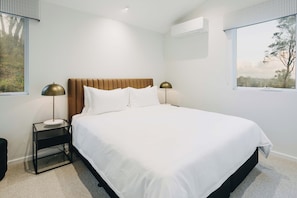 Une chambre moderne avec un grand lit, deux tables de chevet avec des lampes, une fenêtre donnant sur un beau paysage et un appareil de climatisation.