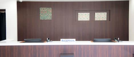 Un mostrador de recepción con un letrero que dice "RECEPTION", dos lavamanos, un escalón pequeño para facilitar el acceso y una cámara de seguridad en el techo.
