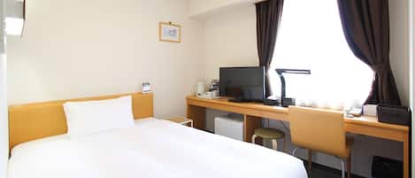 A hotel room with a large bed, a desk with a computer, a chair, and a window with curtains.
