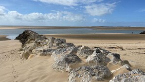 Una spiaggia con grandi rocce in primo piano e una vasta area sabbiosa che si estende fino all'acqua.