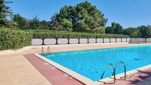 A rectangular swimming pool with clear blue water, surrounded by a concrete deck and a low hedge.
