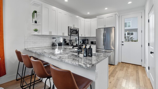 A modern kitchen with white cabinets, a granite countertop, stainless steel appliances, and a wooden floor.