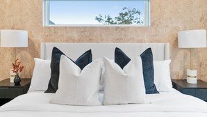 A bedroom with a large bed, two bedside tables, and a window with a view of trees.