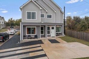 Ein zweistöckiges Haus mit überdachter Terrasse, Auffahrt und umzäunter Garten.