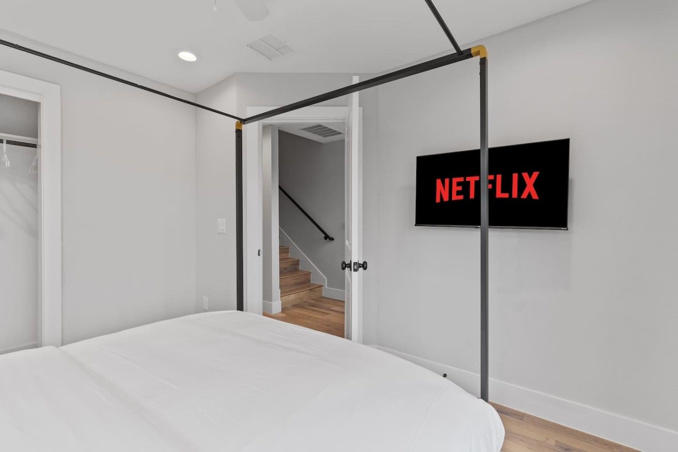 A bedroom with a bed, a door, a staircase, and a wall-mounted TV displaying the Netflix logo.