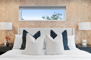 A bedroom with a bed, pillows, a nightstand, a lamp, and a window with a view of trees.