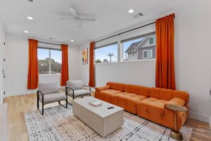 Ein modernes Wohnzimmer mit einer Couch, zwei Sesseln, einem Couchtisch und einem Deckenventilator.