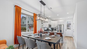 A modern kitchen with white cabinets, a stainless steel refrigerator, and a dining area with a wooden table and chairs.